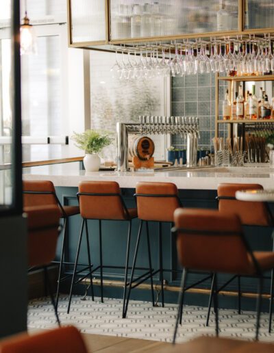 A bar in a restaurant with stools and wine glasses.