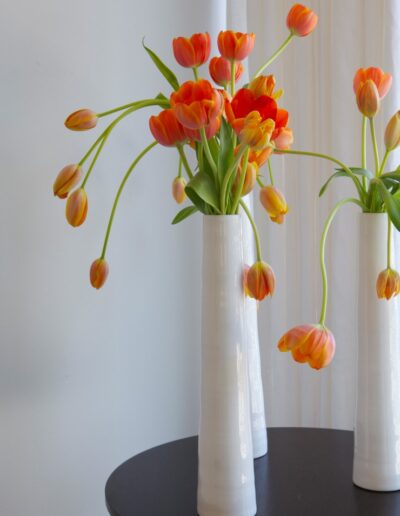 Three white vases with orange flowers on a table.