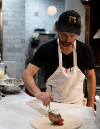 A man in a black apron preparing a pizza.