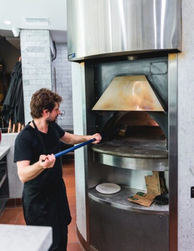 A man in a black apron preparing a pizza in an oven.