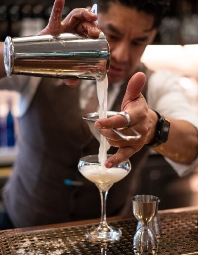 A bartender pouring a cocktail into a glass.