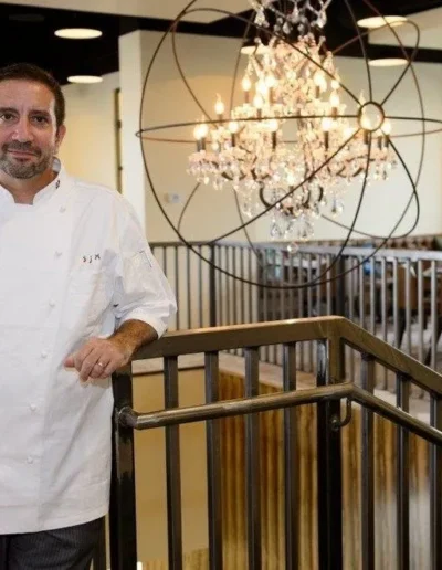 A chef standing in front of a chandelier in a restaurant.